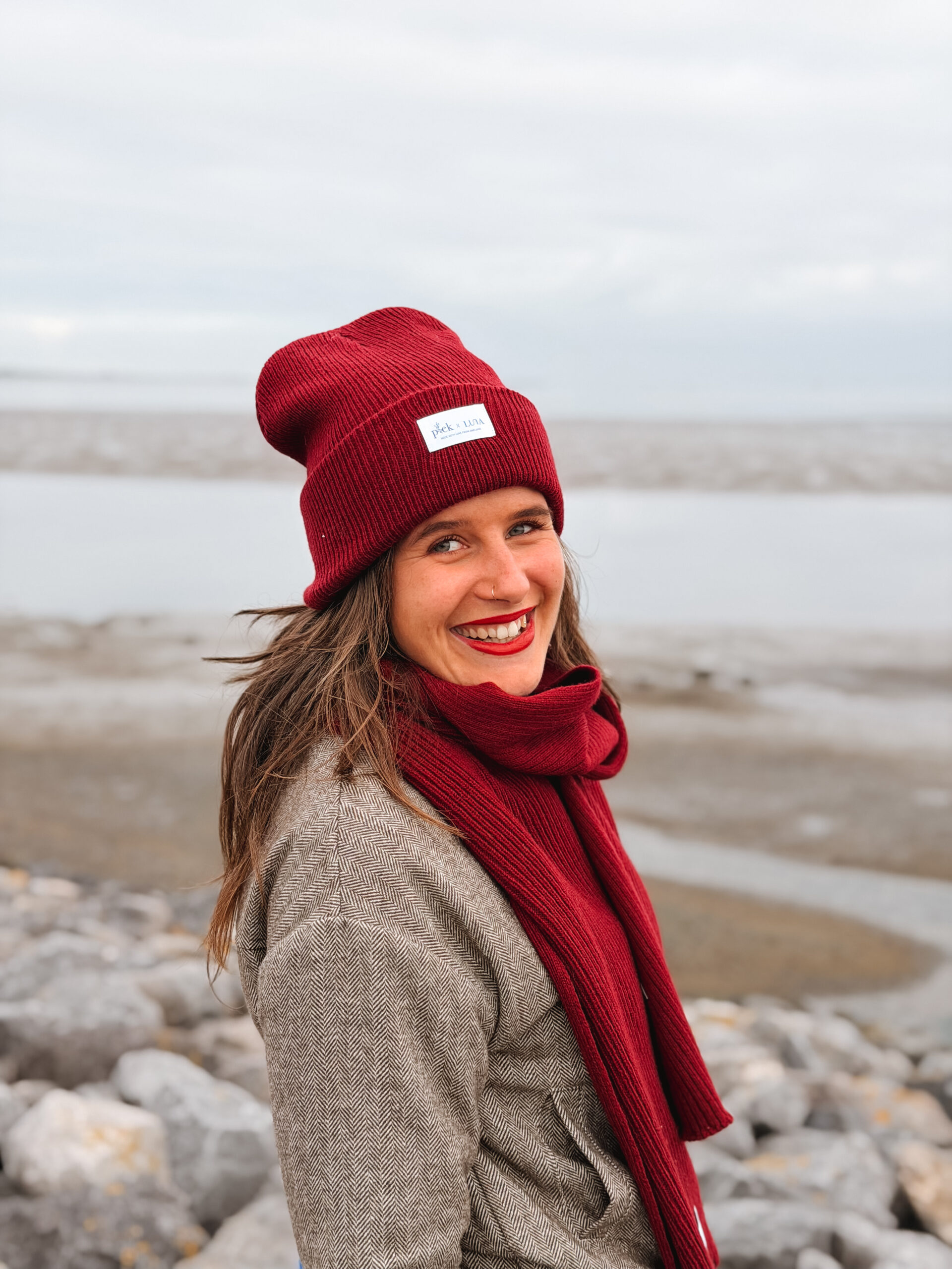 Model in muts, sjaal en jas van Plek & Luna op het strand van Ameland
